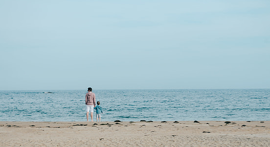 person and toddler standing on seashore during daytime thumbnail