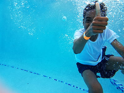 man wearing white top and blue shorts underwater photography thumbnail