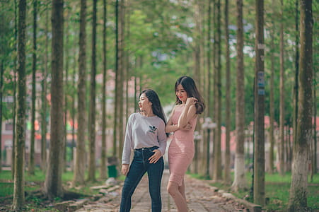 Woman in Pencil Dress Beside Woman in Gray Sweatshirt and Blue Jeans Standing on Pathway thumbnail