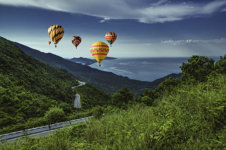 five assorted-color hot air balloon passing through mountains thumbnail