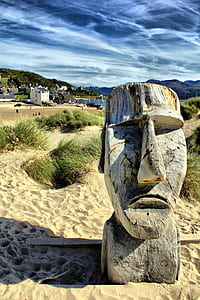 gray wooden human face statue on sand during daytime thumbnail