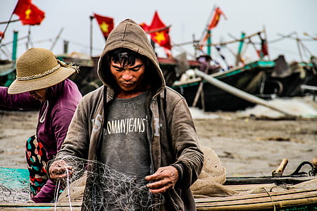 man in black crew-neck shirt and gray zip-up hoodie holding fishing net at daytime thumbnail