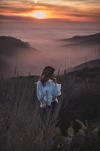 shallow focus photo of woman standing on grass fields under orange sunset thumbnail
