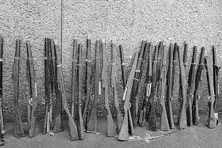 grayscale photo of rifles leaning on wall thumbnail