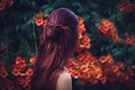 woman with red hair facing away towards red flowers thumbnail