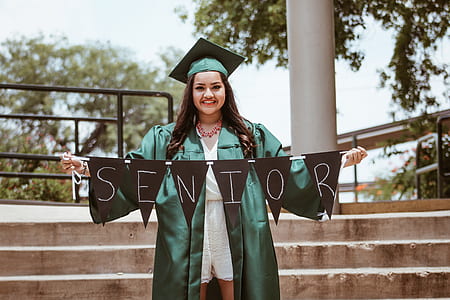 woman wearing green academic dress holding Senior banner during daytime thumbnail
