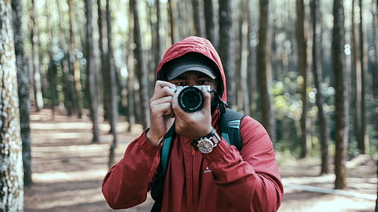 man holdin camera standing between trees during daytime thumbnail