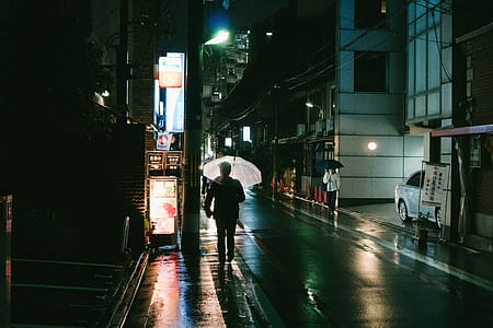 man walking holding umbrella between concrete buildings thumbnail