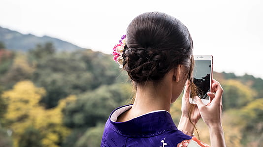 woman holding iPhone capturing mountain during daytime thumbnail