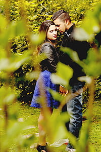 selective focus photography of two couple standing near bush thumbnail