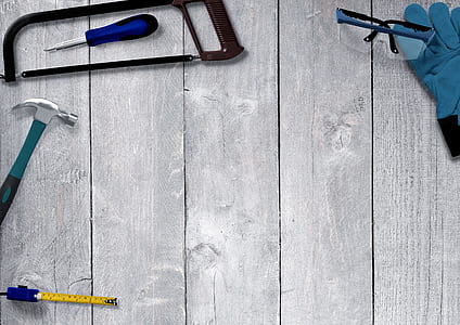 black framed safety glasses, black hacksaw, gray claw hammer, and yellow measuring tape on top of gray board thumbnail