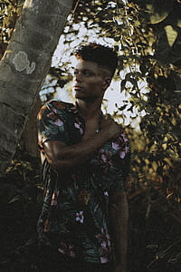 man wearing floral shirt near tree holding left shoulder looking right thumbnail