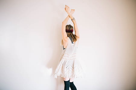woman in white lace sleeveless mini dress and black knee-high socks rising hand facing white painted wall thumbnail