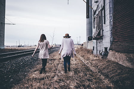 two women walking on grass field beside train rails thumbnail