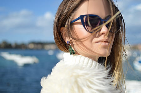 selective focus photography of woman wearing blue framed black lens sunglasses and white fur-lined coat thumbnail