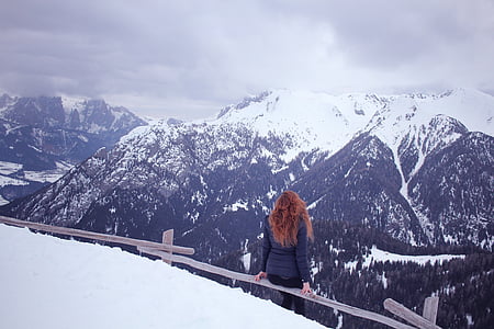 woman sitting on brown fence in front of mountain at daytime thumbnail