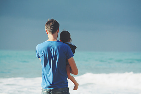 man in blue shirt carrying baby beside seashore thumbnail