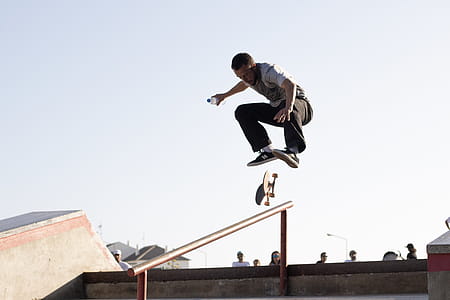 Man Wearing White T-shirt Performing Skateboard Tricks on Rail Under Blue Sky thumbnail