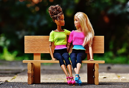 two Barbie dolls sitting on brown wooden bench miniature thumbnail