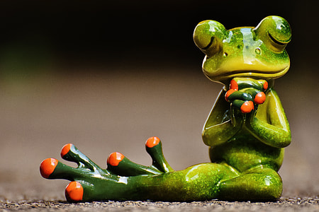 shallow photography of ceramic praying frog sitting on gray concrete flooring thumbnail