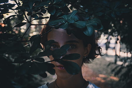 woman standing behind green plants during daytime thumbnail