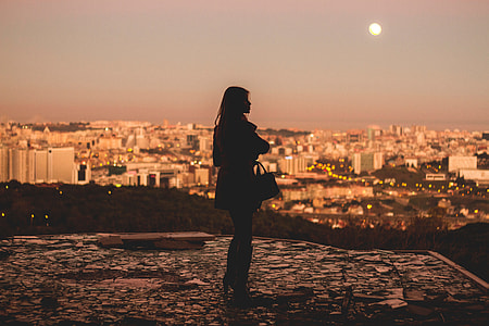 silhouette of woman near city during yellow sunset thumbnail
