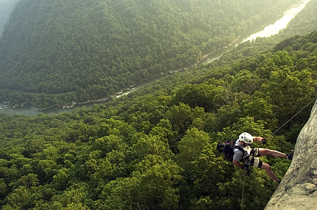 man climbing on cliff with trees below thumbnail