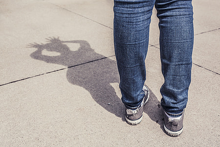 person's shadow wearing blue jeans and pair of gray sneakers thumbnail