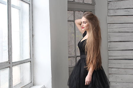woman wearing black dress standing near window thumbnail