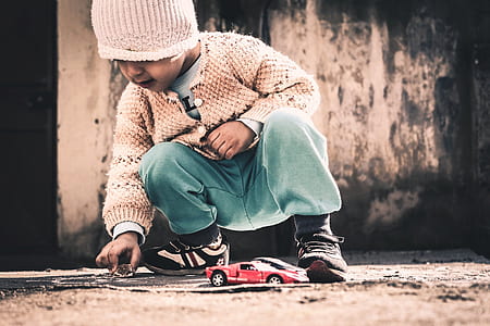 boy playing red sports car beside gray wall thumbnail