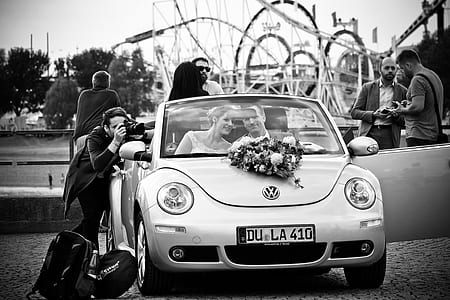 grayscale photography of brides and groom riding on Volkswagen Beetle convertible coupe thumbnail