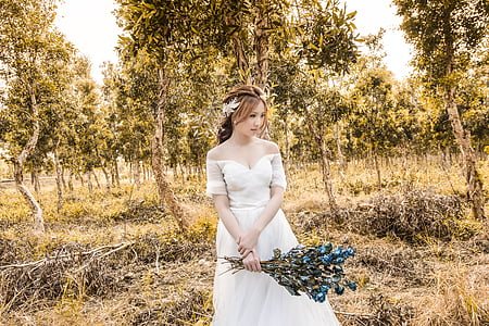woman standing on a grass field while holding a bouquet of blue flowers thumbnail