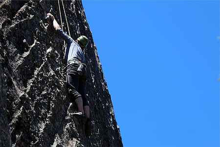 man climbing rock cliff under blue sky thumbnail