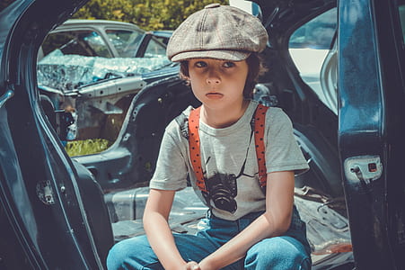 boy sitting inside wrecked black vehicle body shell during daytime thumbnail