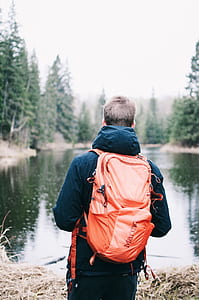 man with bag in front of lake near trees thumbnail