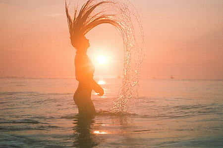 silhouette woman standing in shallow body of water during golden hour thumbnail