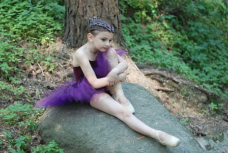 girl wearing purple tutu ballerina dress sits on gray rock thumbnail