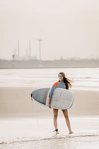 woman holding white and blue surfboard standing near shore thumbnail