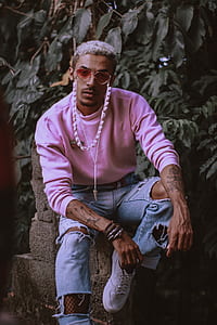 man wearing sweatshirt with tattoo sitting on concrete surface thumbnail