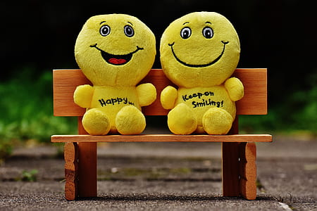 two yellow emoticon plush toys sitting on brown wooden bench thumbnail