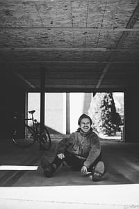 man in jacket sitting on floor near bike thumbnail