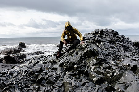 Selective Color Photography of Man Wearing Hoodie on Stone Behind Body of Water thumbnail