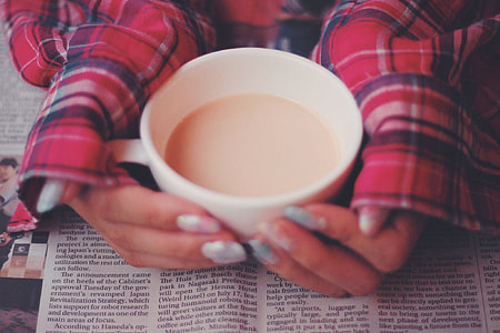 person in red tops touching filled white ceramic mug on top of newspaper thumbnail