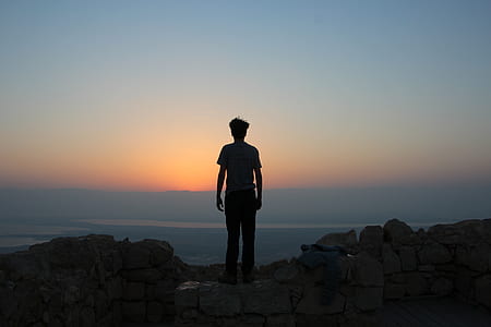silhouette of man standing mountain rock facing the sun during golden hour thumbnail