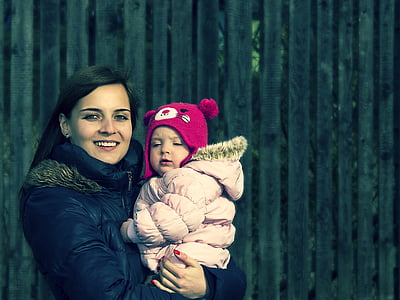 smiling woman carrying child near brown wooden fence thumbnail