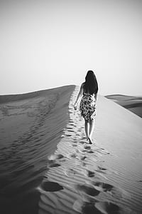 grayscale photo of woman barefoot walking on sand thumbnail