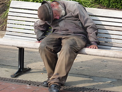 man in gray dress shirt and pants sleeping in gray wooden bench during daytime thumbnail