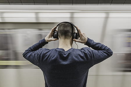 man wearing gray sweatshirt holding headphones in front on train station thumbnail