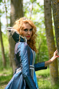 woman wearing blue medieval dress near tree trunks thumbnail