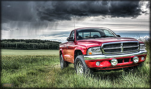 red Dodge truck on grass land under cloudy sky thumbnail